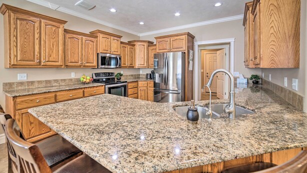 A kitchen with granite countertops, stainless steel appliances, wooden cabinets, and a central island with a sink. - Spacious Idaho Home: Ski, Hike, & Fish! (Rexburg)