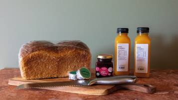 A loaf of bread, two bottles of juice, a jar of jam, and a knife on a cutting board.