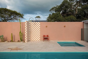 Una piscina con un muro a cuadros, una silla roja y cactus.