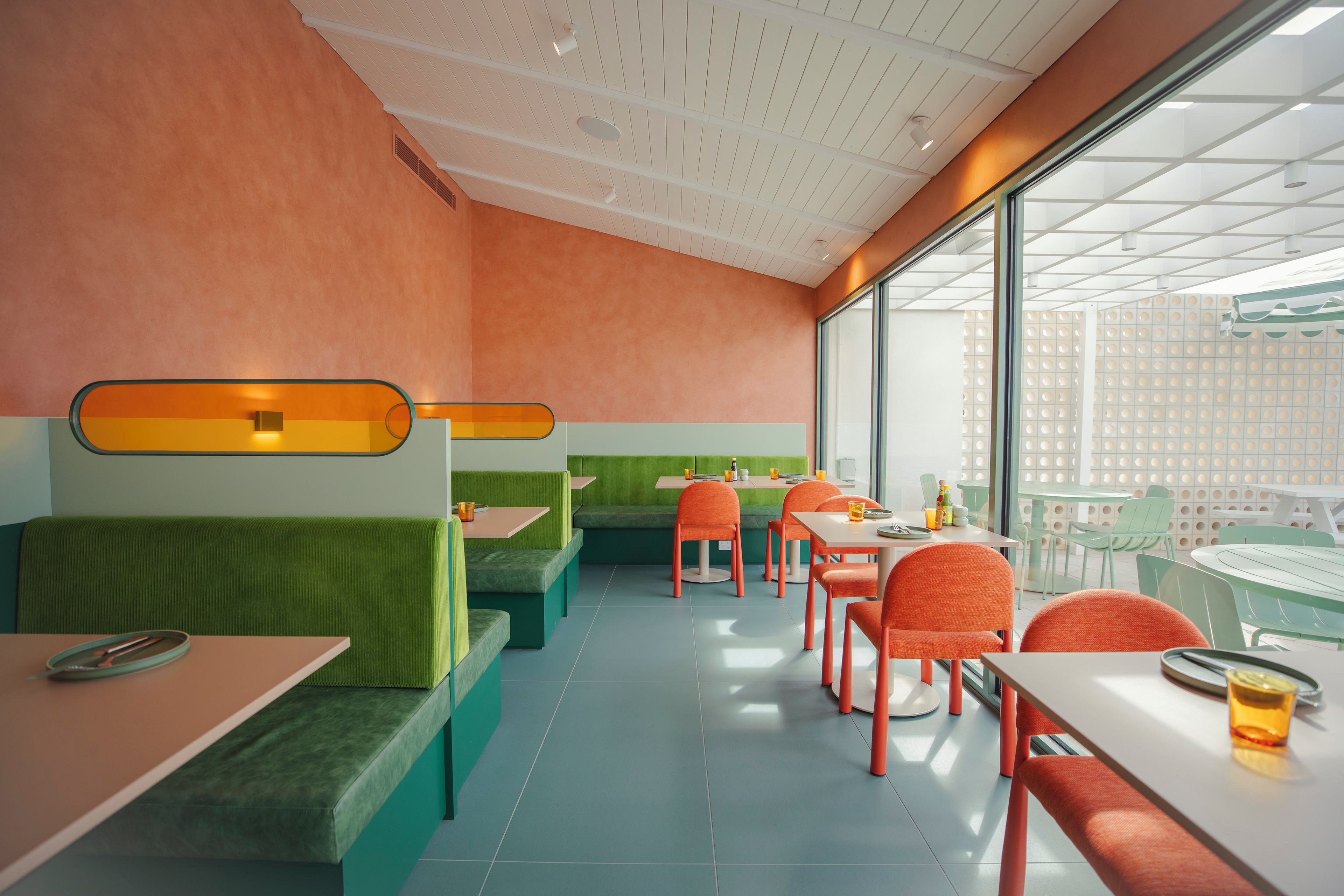 Un restaurante moderno con asientos verdes y naranjas, ventanas amplias y un techo alto.