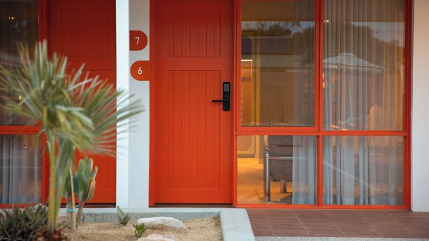 A red door with the number 7, a glass door with curtains, and a small plant in the foreground. - The Monty (Anglesea)