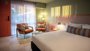 A hotel room with a large bed, two armchairs, a small table, and a nightstand with a lamp. - The Monty (Anglesea)