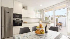 A modern kitchen with white cabinetry, a stainless steel refrigerator, and a dining area with a table set for two. - 3 bedroom house near the sea (Can Picafort)