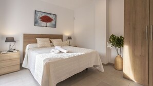 A neatly arranged bedroom with a bed, bedside tables, a nightstand, a wooden wardrobe, and a wall-mounted painting. - 3 bedroom house near the sea (Can Picafort)