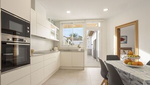 A modern kitchen with white cabinetry, a Bosch oven, and a dining area with a table set for two. - 3 bedroom house near the sea (Can Picafort)