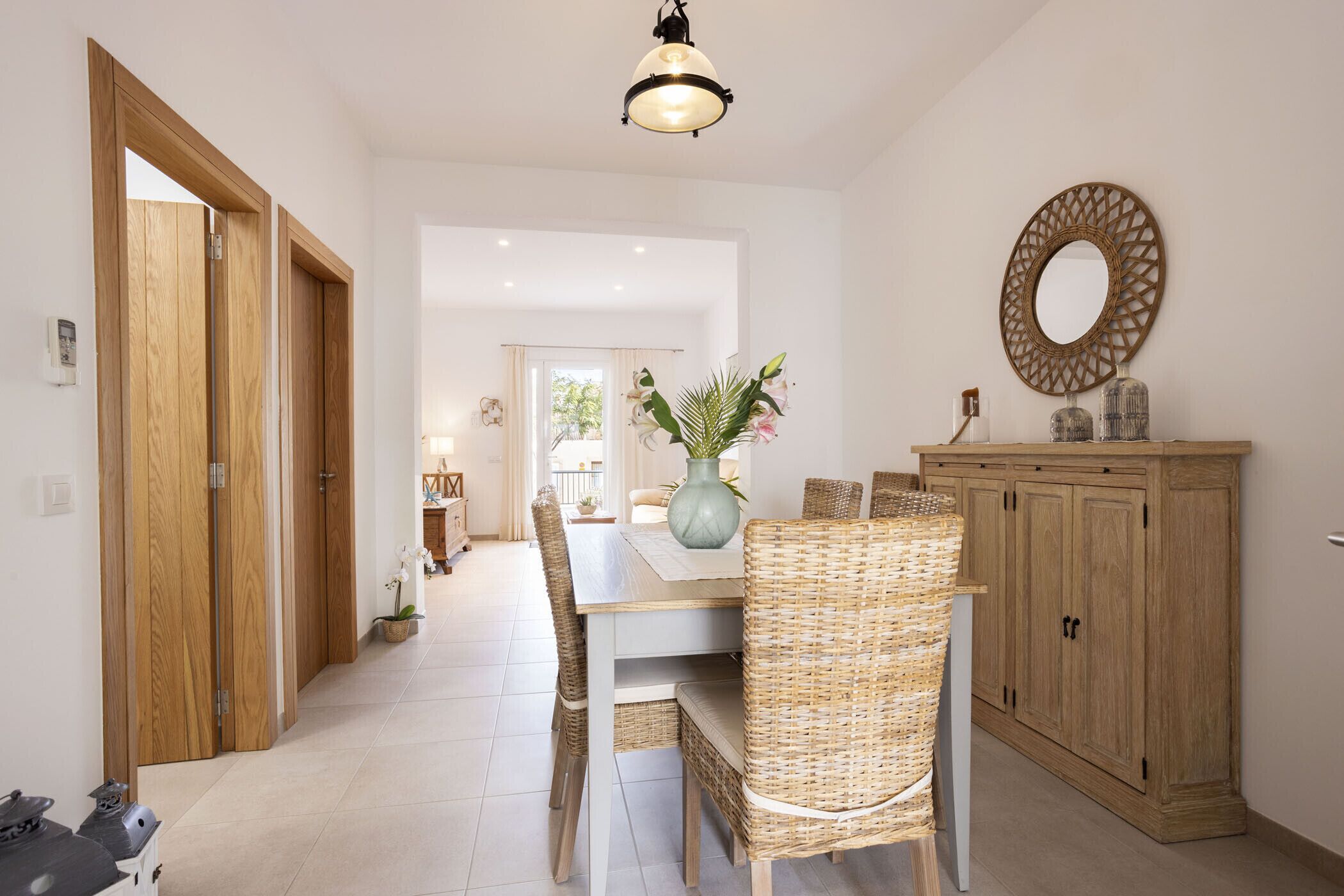 A dining area with a wooden cabinet, wicker chairs, a table, and a hanging light fixture.