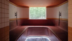 Un jacuzzi con vistas a árboles a través de una ventana, paredes con azulejos e iluminación empotrada en el techo.