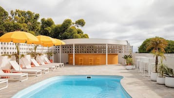 A swimming pool with lounge chairs and umbrellas, a covered seating area, and a building with a unique circular design.