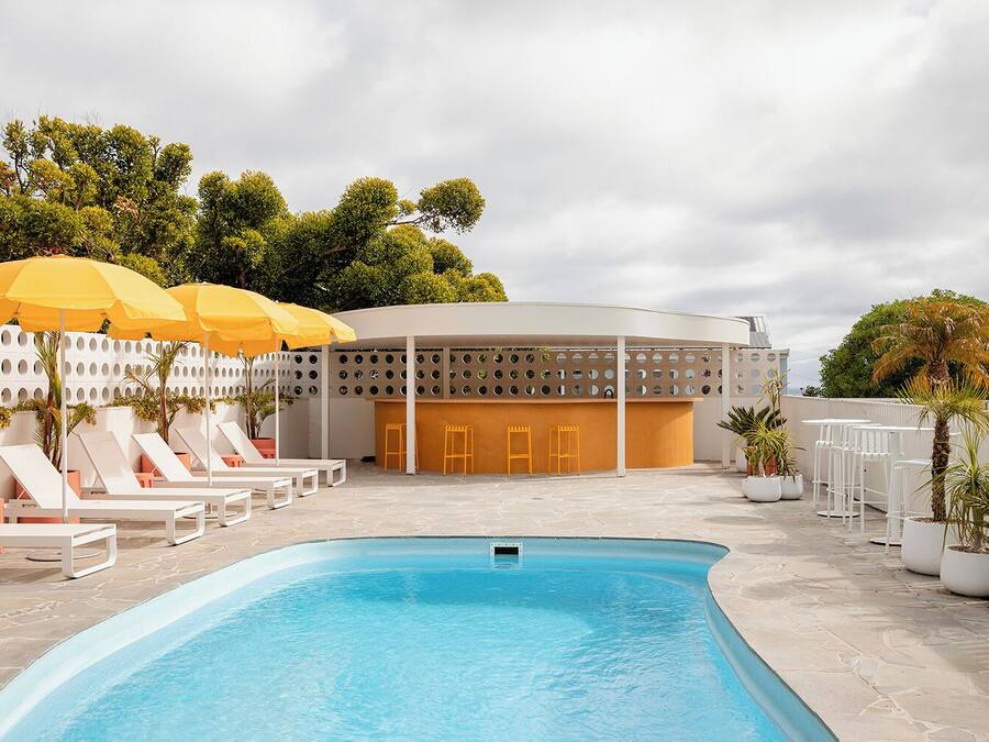 A swimming pool with lounge chairs and umbrellas, a covered seating area, and a building with a unique circular design.