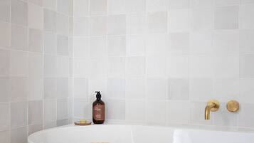 A bathroom with a white bathtub, a towel, and a bottle of shampoo on the floor.