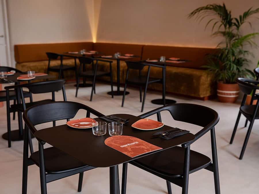 Un restaurant avec des tables et des chaises noires, un canapé et une plante en pot.