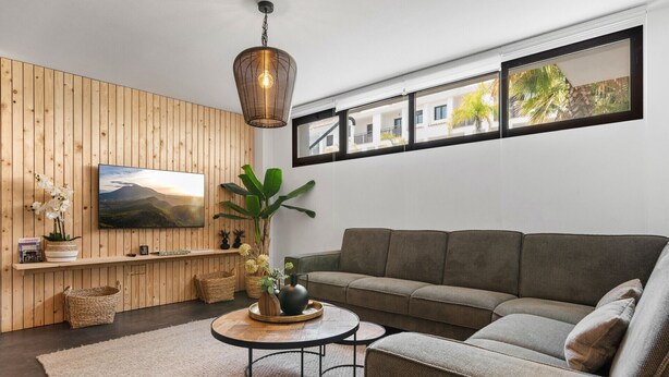 A modern living room with a wooden panel wall, a grey sofa, a round coffee table, and a hanging light fixture. - El Sembrador | Pool - terrace - pool table (La Cala de Mijas)