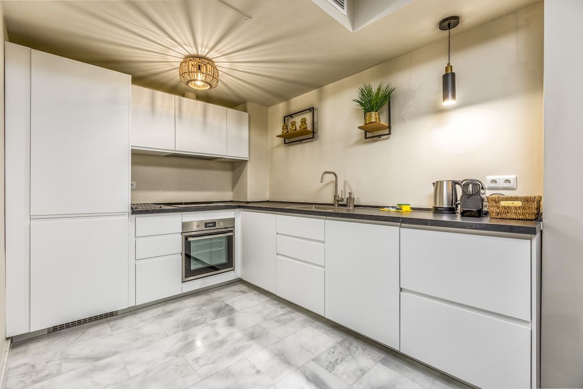 A modern kitchen with white cabinetry, a built-in oven, a sink, and a pendant light.