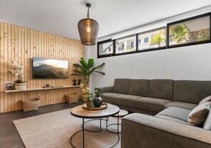 A modern living room with a wooden panel wall, a grey sofa, a round coffee table, and a hanging light fixture. - El Sembrador | Pool - terrace - pool table (La Cala de Mijas)