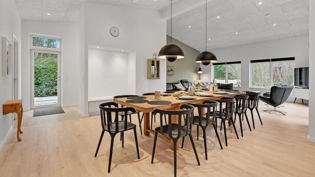 Ett rymligt matområde med ett träbord och svarta stolar, stora fönster och en modern takdesign.