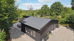 Ett modernt hus i två våningar med ett mörkt tak och mörka ytterväggar, omgivet av frodig grönska och träd.