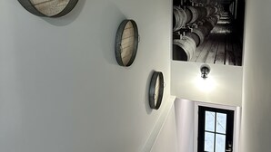 A staircase with a view of wine barrels in the background, a wooden barrel wall art piece, and a door at the bottom.