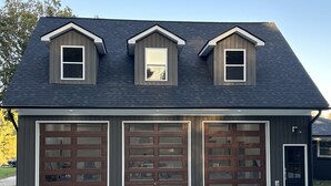 A two-story building with three garage doors and a small dormer window on the roof.