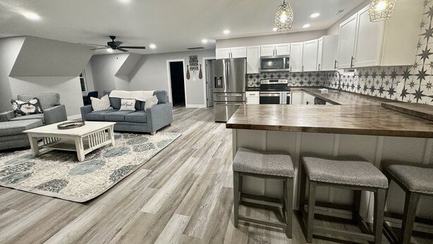 A modern kitchen with white cabinets, a wooden island with bar stools, and a gray sofa in the living area.