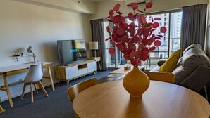 A modern hotel room with a round wooden dining table, a flat-screen TV, a sofa, and a large window with curtains. - Pandanas Apt 1 (U will love it) (Darwin City)