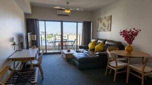 A modern hotel room with a sofa, a dining table, and a chair. There is a large window with a view of buildings outside. - Pandanas Apt 1 (U will love it) (Darwin City)