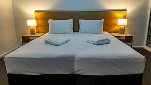 A double bed with white linens, two pillows, and two folded towels on each side. There are two bedside lamps on either side of the bed. - Pandanas Apt 1 (U will love it) (Darwin City)