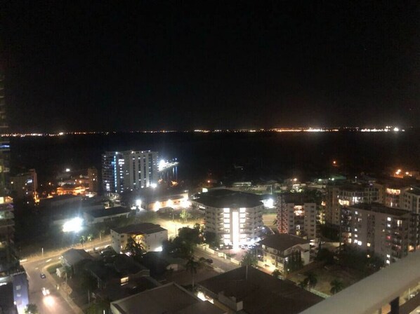 A nighttime cityscape with illuminated buildings and a distant view of a body of water. - High Above, Pandanas Darwin 21st floor with views (Darwin City)
