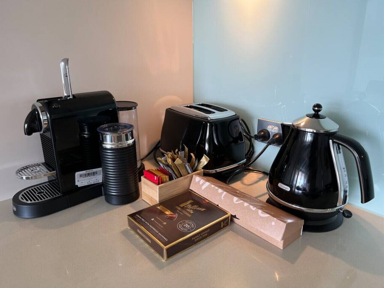 Een keukentafel met een koffiezetapparaat, broodrooster, waterkoker en een doos koffiebonen.