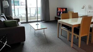 Un salon moderne comprenant un canapé, une table basse en verre, une table à manger avec des chaises, un téléviseur et un ventilateur de plafond.
