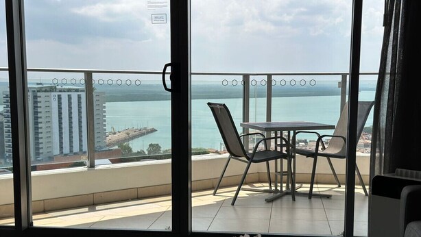 Un balcone con tavolo e sedie, affacciato su uno specchio d'acqua e degli edifici.