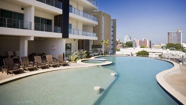 A modern hotel with a swimming pool, lounge chairs, and a cityscape view.