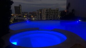 A swimming pool with a blue-lit edge, surrounded by a building complex.