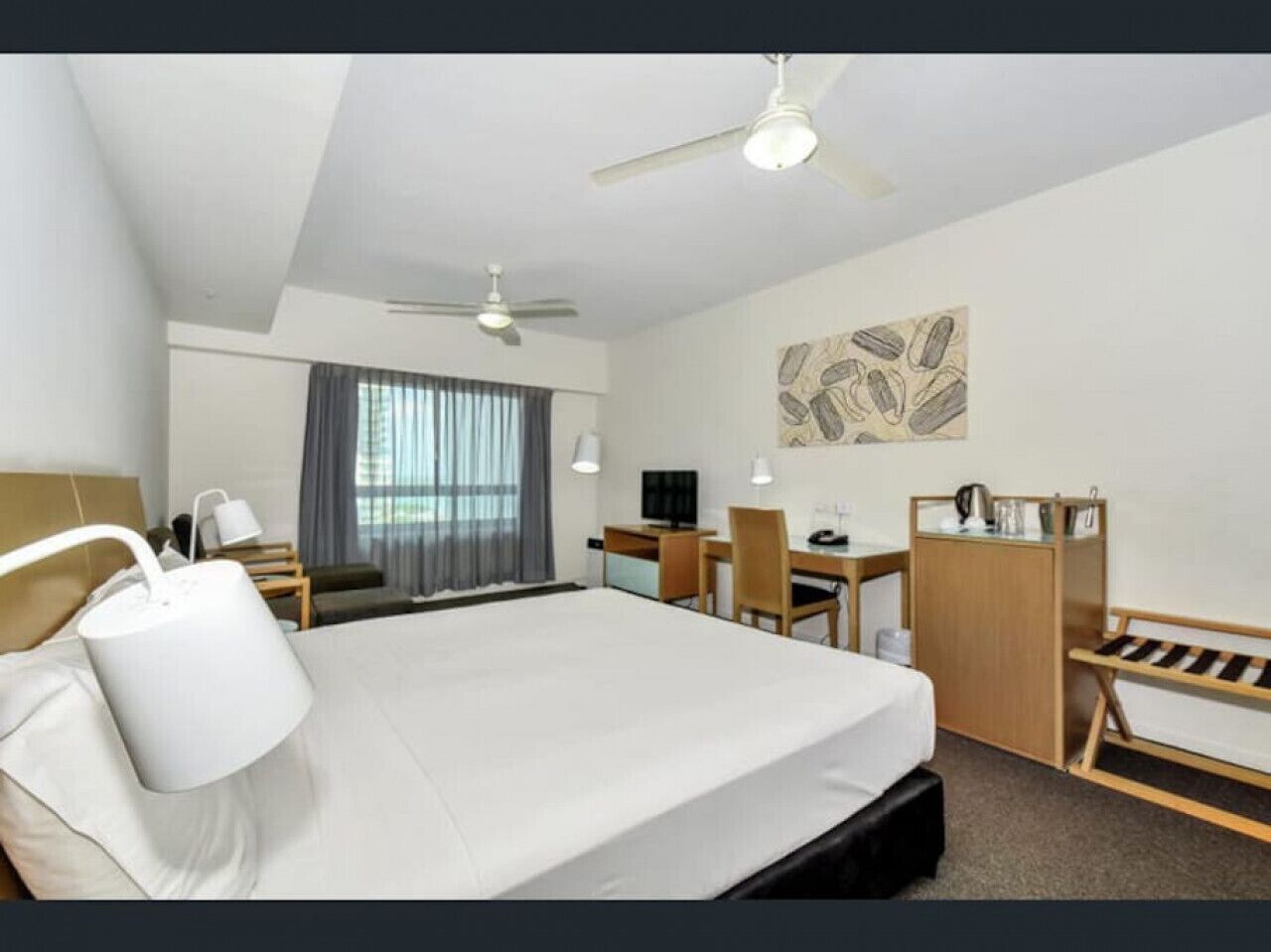 Een hotelkamer met een bed, bureau, stoel, kledingkast en plafondventilatoren.