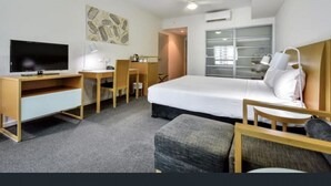 A hotel room with a bed, a desk, a chair, a television, and a window.