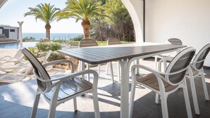 Eine Terrasse im Freien mit Tisch und Stühlen, Blick aufs Meer und Palmen.