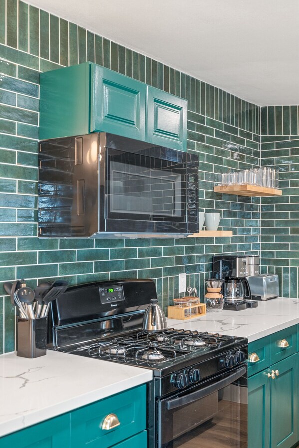 Une cuisine avec des armoires de couleur turquoise, un poêle noir, un four à micro-ondes et une machine à café.