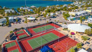 Vista aérea de una zona residencial costera con varias canchas de tenis, un puerto deportivo y casas con vistas al océano.