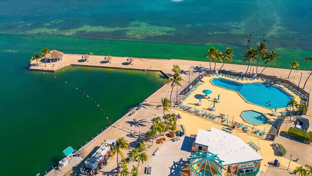 Vista aérea de un resort con una piscina grande, palmeras y un muelle.