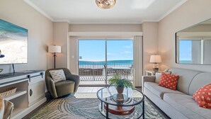 Un salon moderne avec une table basse en verre, un canapé, un fauteuil, un bureau et une grande fenêtre donnant sur la plage.