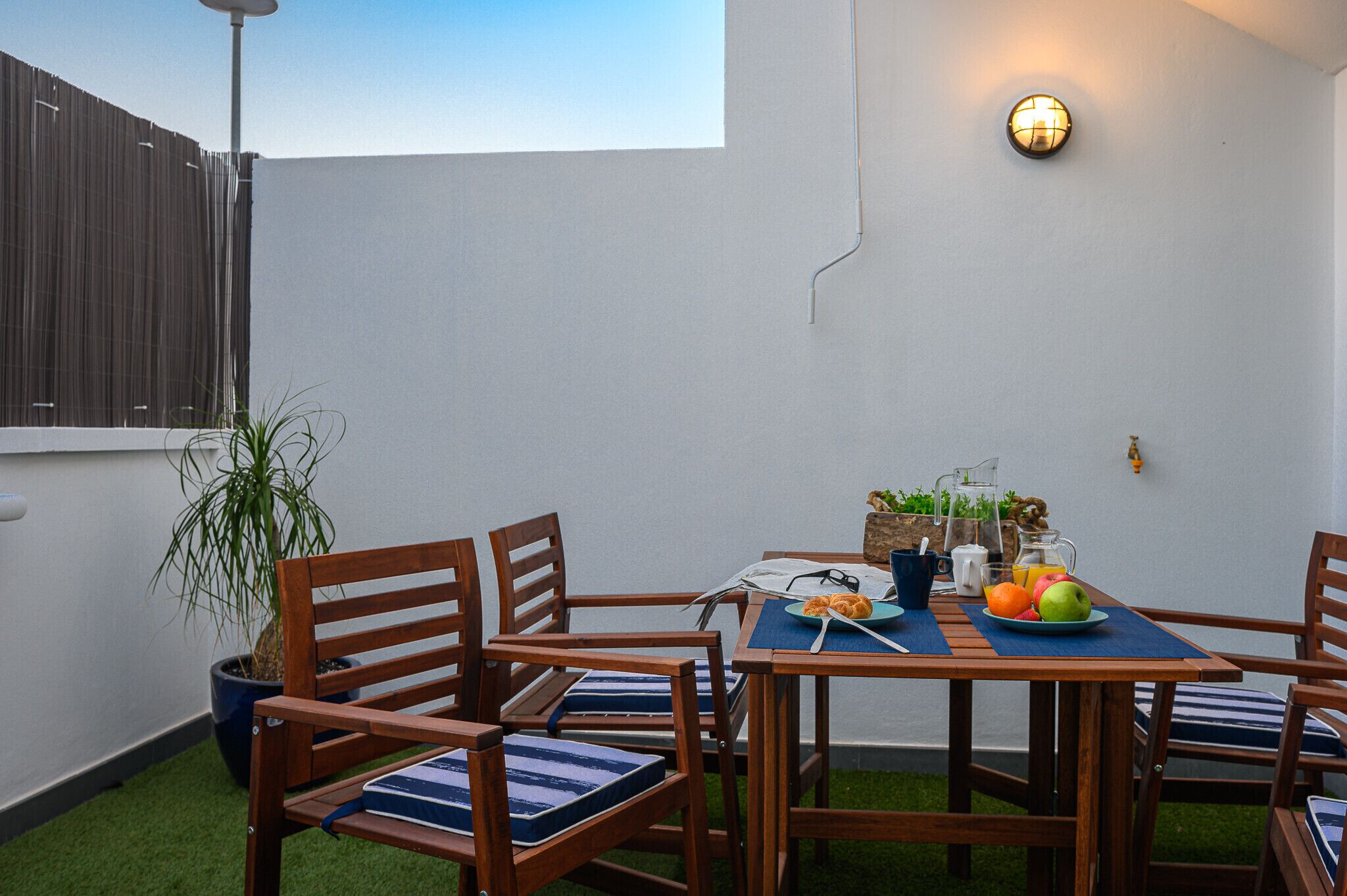 Une terrasse avec une table dressée pour le petit-déjeuner, entourée de chaises en bois avec des coussins bleus.