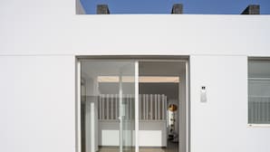 A modern building entrance with a glass door, a white exterior, and stone chimneys.