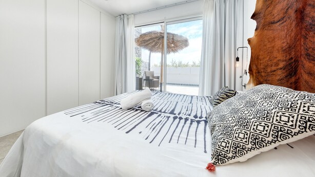 A modern hotel room with a large bed, a view of the outdoors, and a unique wooden accent wall.