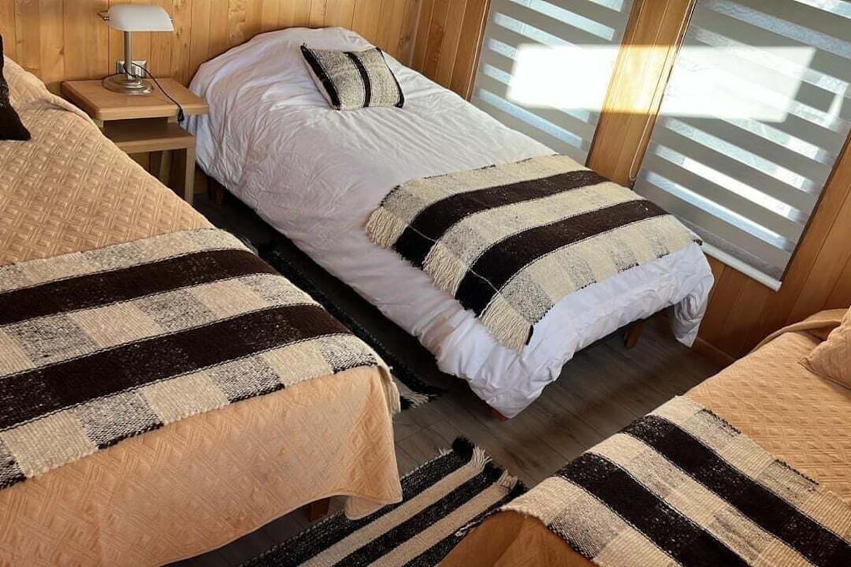 A room with two beds, a nightstand, and a window with blinds.