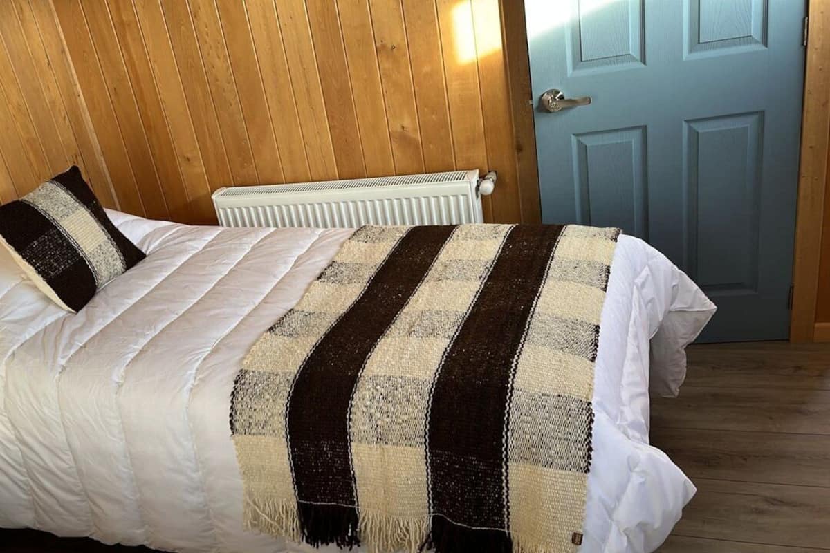 A bed with a white comforter and striped blanket, a white radiator, and a wooden wall with a blue door.