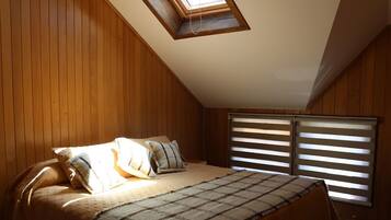 Une chambre avec des lambris en bois, un puits de lumière, un lit avec des oreillers et une fenêtre avec des stores.