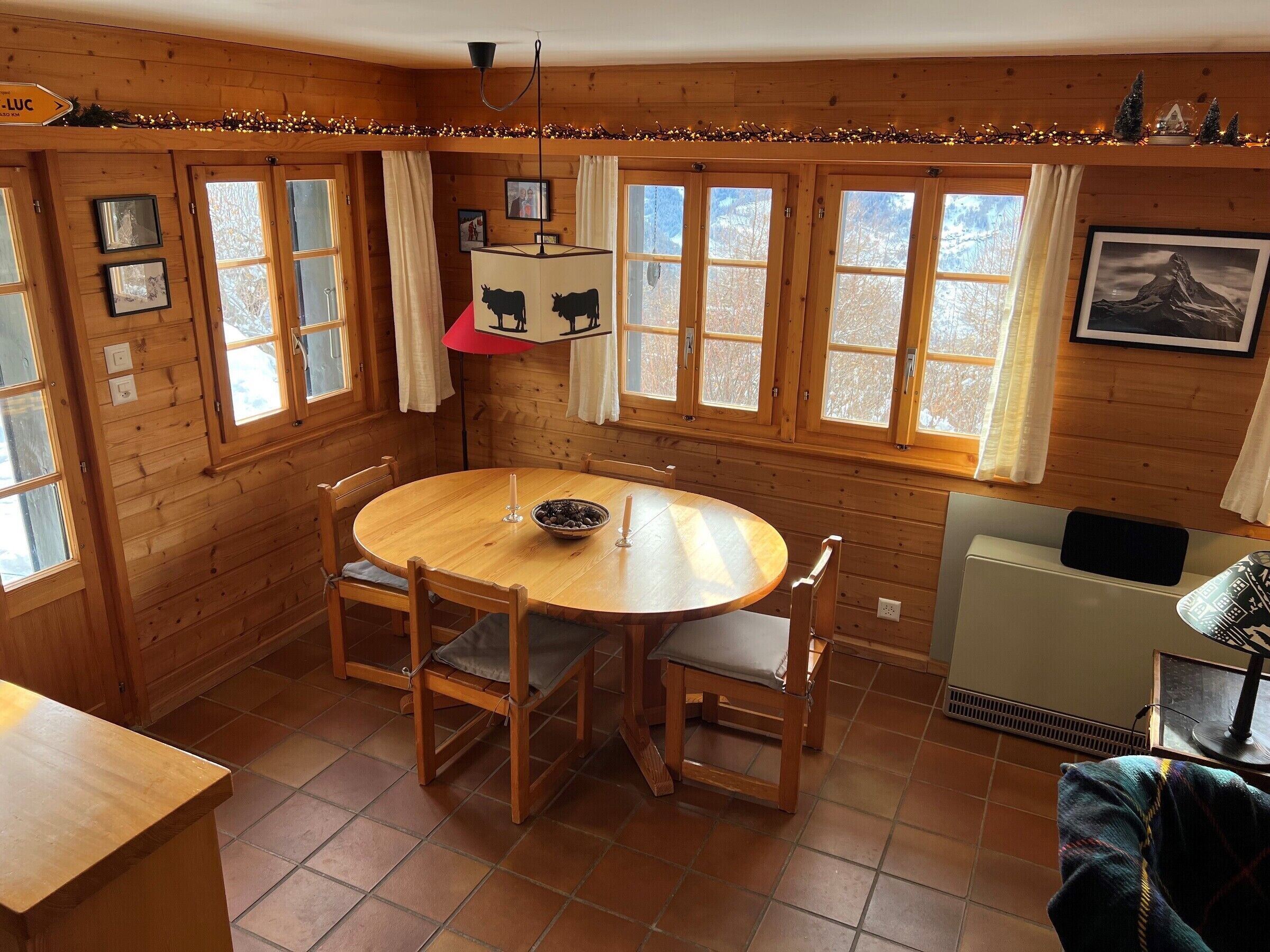 En mysig stuga byggd av trä, med ett runt matbord, stolar och ett litet köksutrymme.