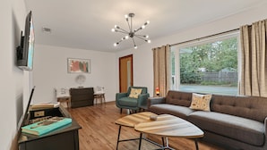 Una sala de estar con sofá, mesa de centro, televisor y ventana con cortinas.
