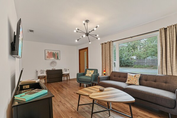 En moderne stue med sofa, sofabord, fjernsyn og en loftlampe.