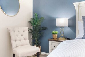 A bedroom with a tufted armchair, a bedside table with a lamp, and a potted plant. - Vansen's Golfshores Inviting, Cozy Condo on Golf Course! (Branson)