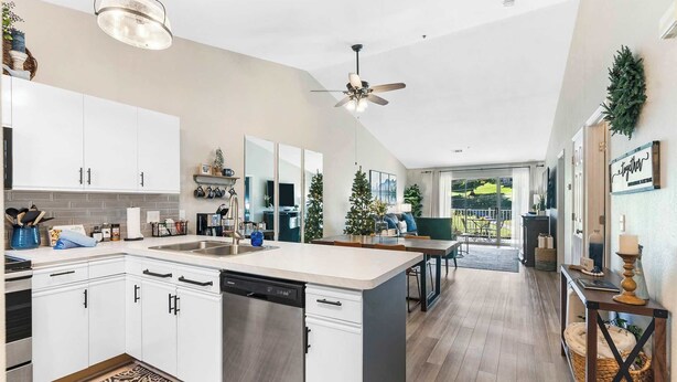 A modern kitchen with white cabinets, a dishwasher, and a large island. There are Christmas trees and a dining area visible in the background. - Vansen's Golfshores Inviting, Cozy Condo on Golf Course! (Branson)